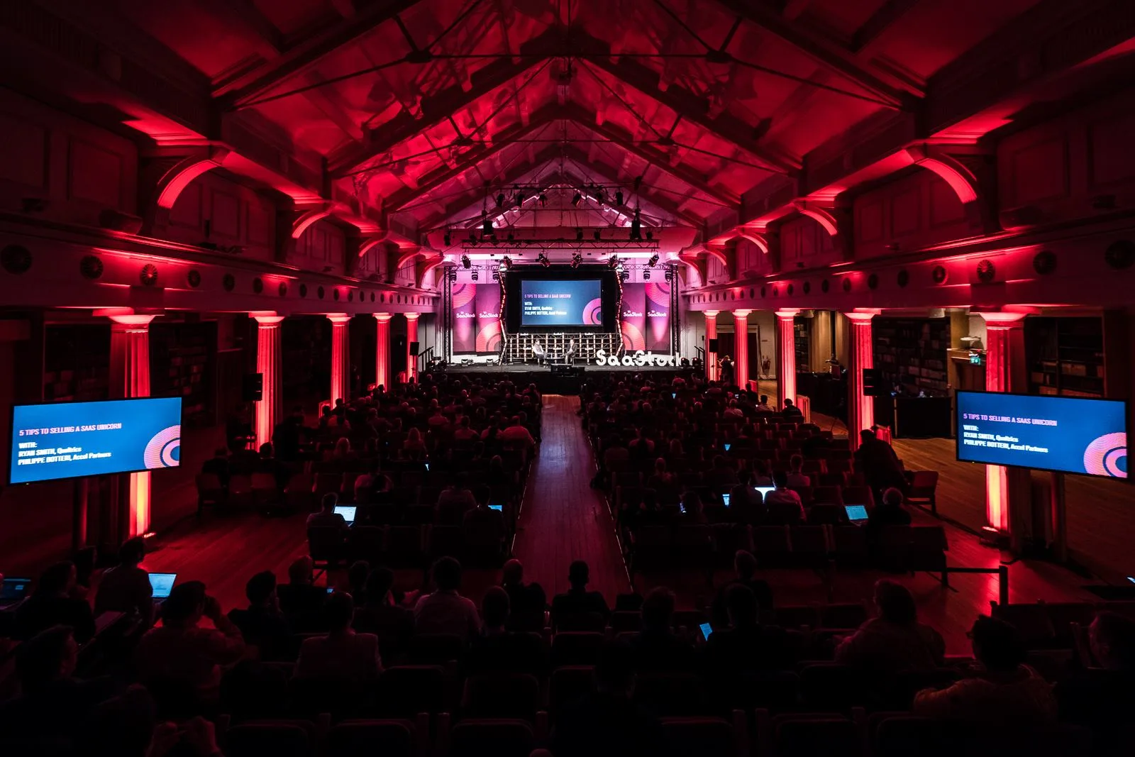Live at SaaStock Europe 2017 — rear-of-house view of the SaaStock mainstage with the '5 Tips to Selling a SaaS Unicorn' slide (Mike Davis, Qualtrics; Philippe Botteri, Accel Partners) on both side screens