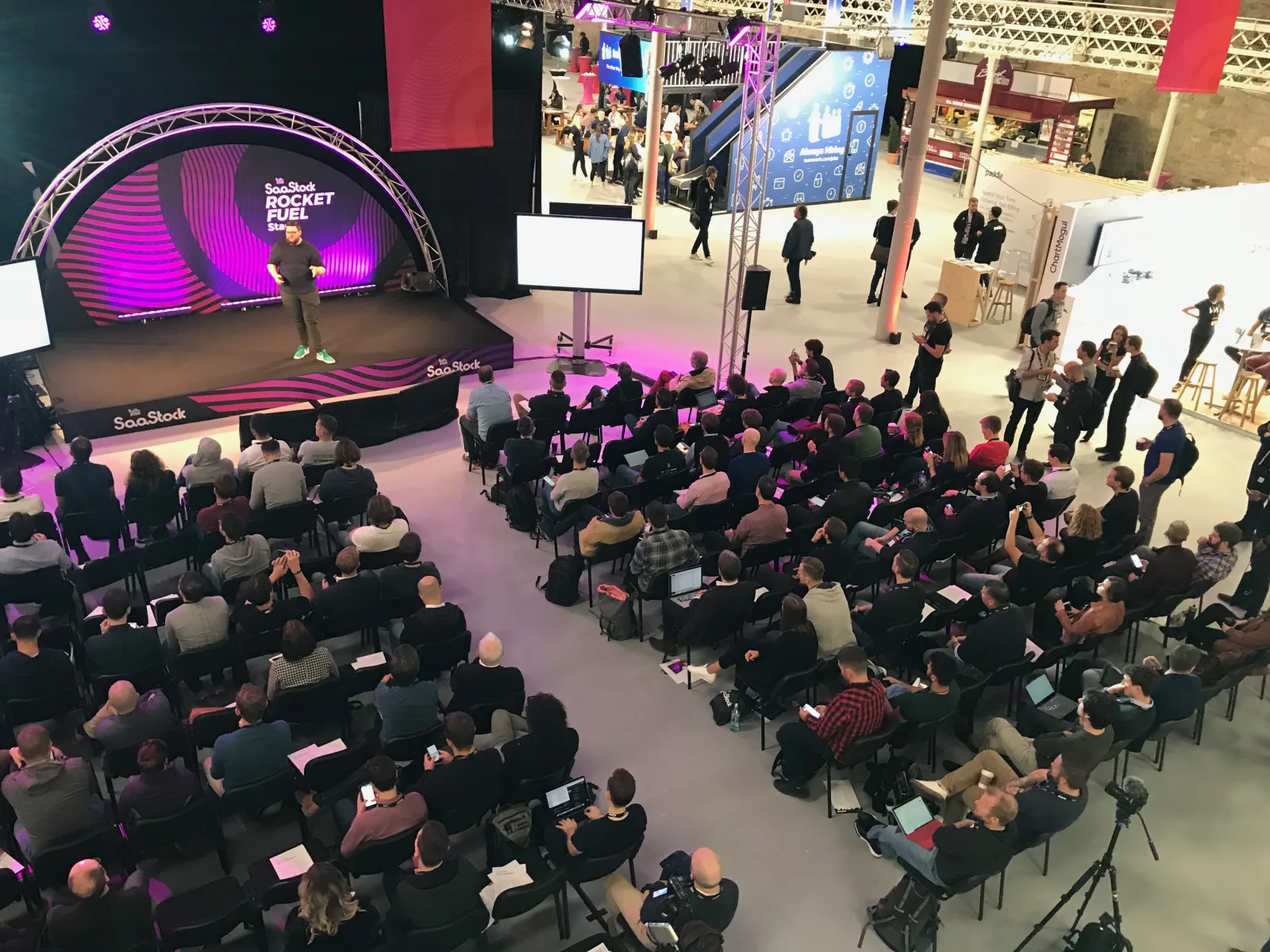 Live at SaaStock Europe 2018 — Rocket Fuel Stage from the balcony, speaker on the curved magenta SaaStock '18 LED set, packed seated audience