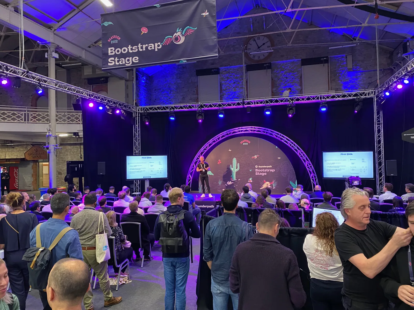 Live during SaaStock Europe 2022 — Bootstrap Stage at standing-room capacity, Founderpath-sponsored cactus-desert set behind the speaker