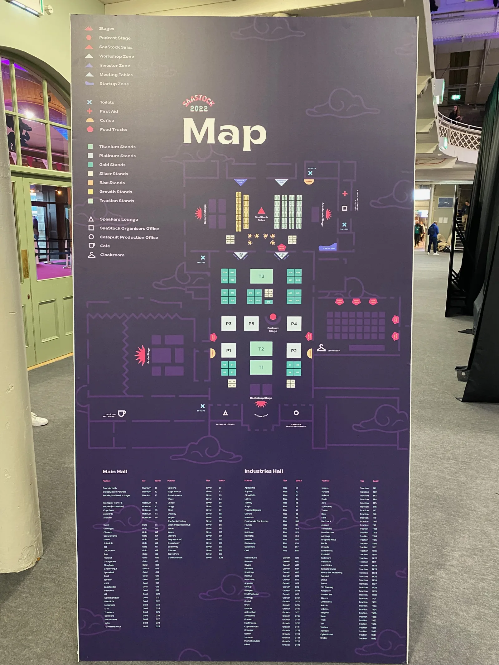 On-site signage at SaaStock Europe 2022 — official SaaStock 2022 floor map standee with Main Hall + Industries Hall booth zones and the full exhibitor list printed beneath