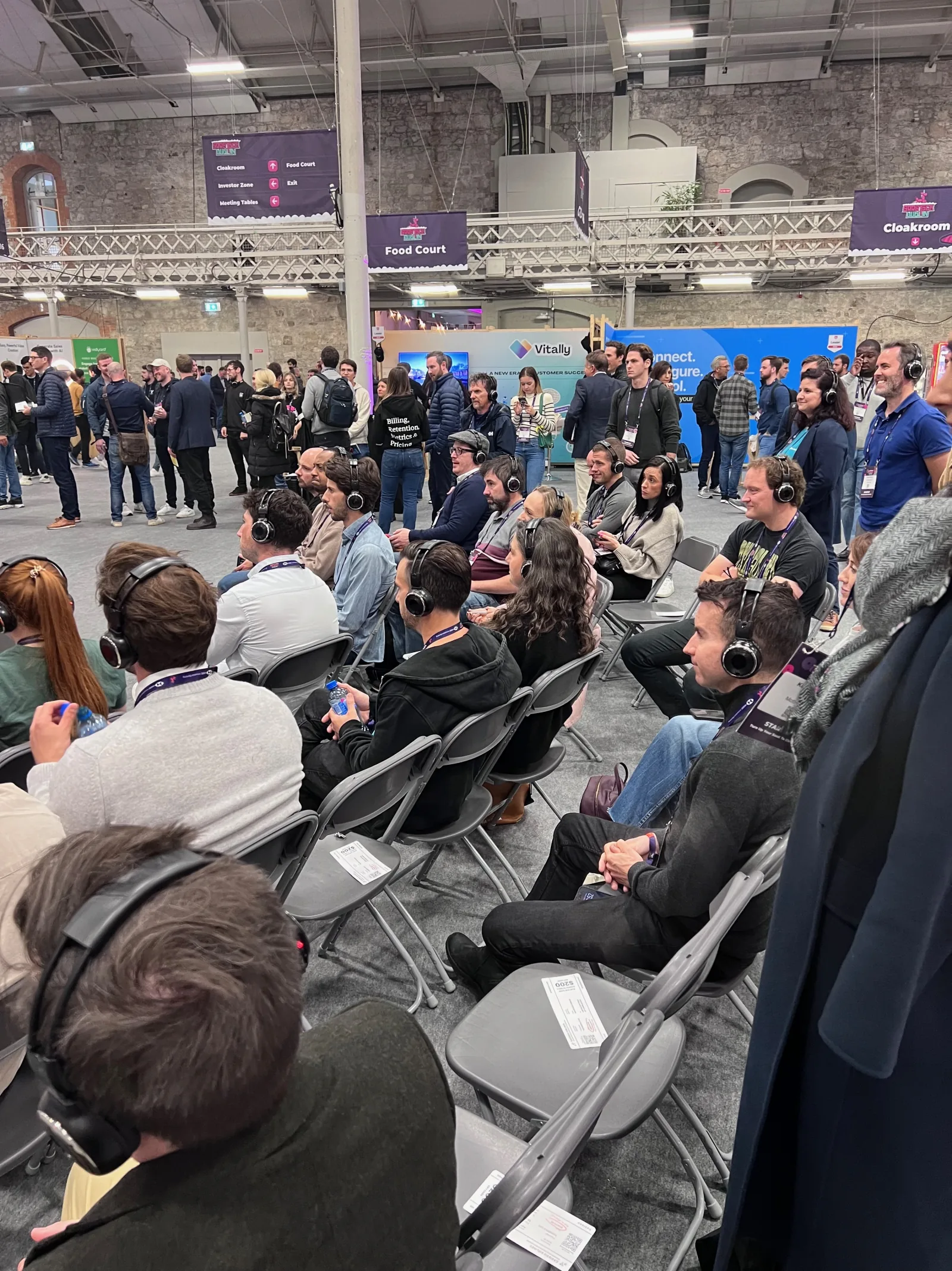 Live at SaaStock Europe 2023 — attendees watching a silent-disco-style session on branded headphones in front of the Vitally booth