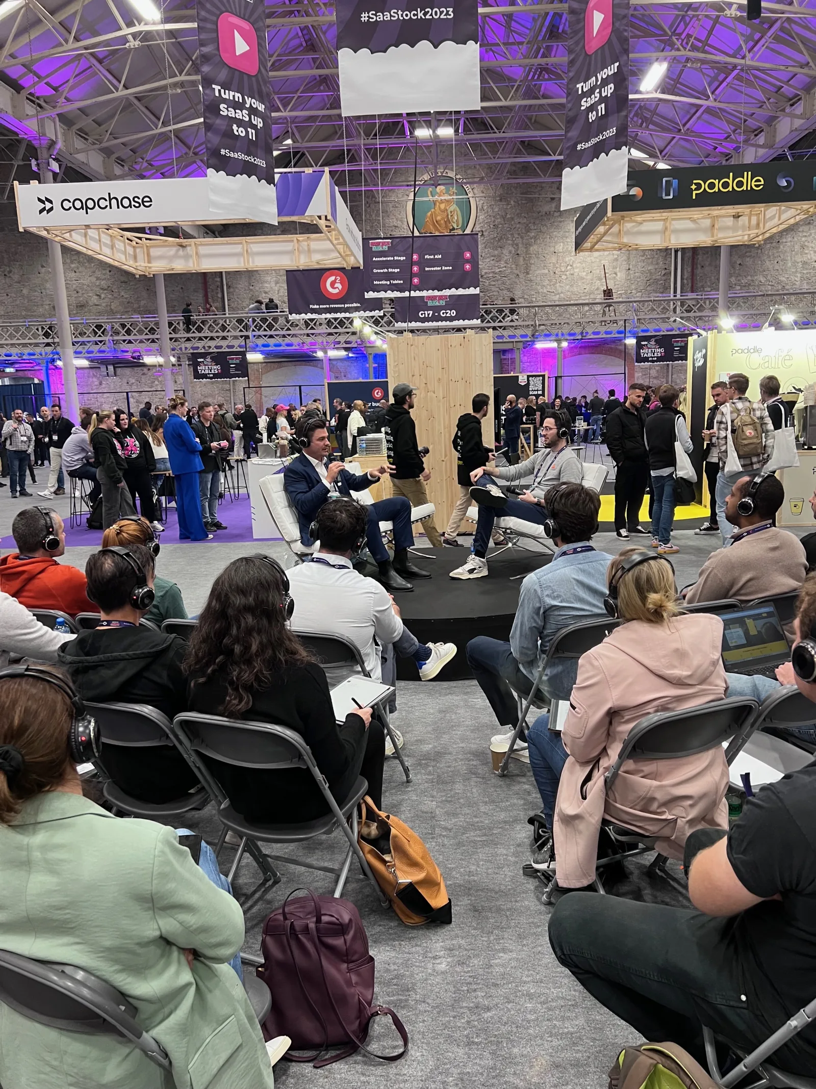 Live at SaaStock Europe 2023 — Podcast Stage panel with three panelists and a full silent-disco audience on headphones