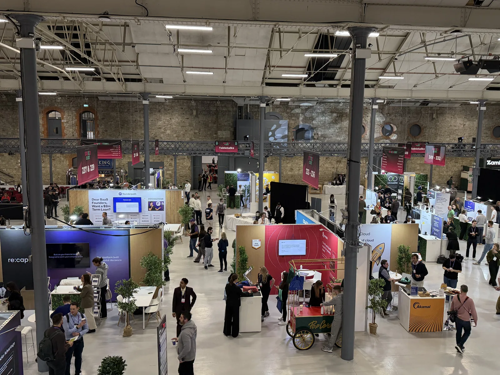 Aerial view of the SaaStock Europe 2025 expo floor with 84 sponsor booths, networking lounges and the Founderpath stand at center