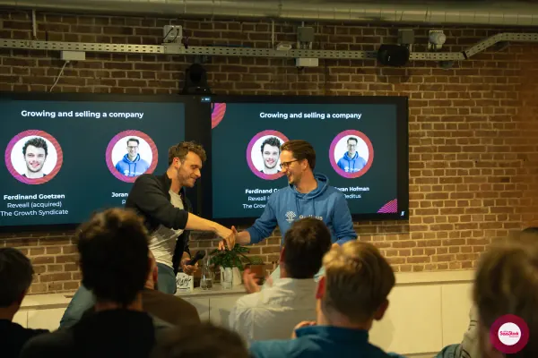 Ferdinand Goetzen and Joran Hofman shake hands on stage at SaaStock Local Amsterdam Q2 2024, in front of the 'Growing and selling a company' slide
