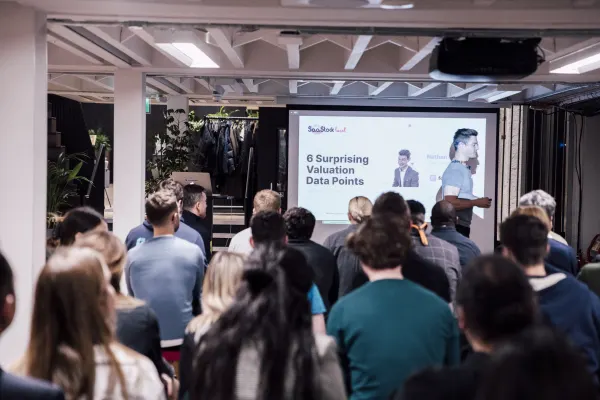 Live at SaaStock Local London — audience watching the 'SaaStock Local · 6 Surprising Valuation Data Points' slide with two speaker headshots on the projected deck