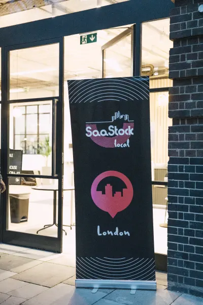 On-site signage — the SaaStock Local London pull-up banner outside the venue door, with the city-skyline logo and 'London' wordmark on a navy background
